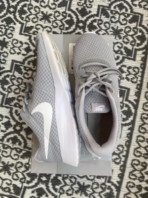 Nike Tanjun Herr Storlek 42 - Snygga grå sneakers från Nike med vit sula och vit swoosh på sidan. Ovandelen är i meshmaterial som andas och skorna har klassisk snörning. Perfekta för dig som gillar en clean och sportig stil. Perfekt skick och inga skador. Skickar samma dag! Pris kan diskuteras