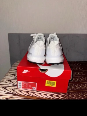 Vita Adidas Ultra Boost sneakers - Säljer ett par fräscha vita Adidas Ultra Boost sneakers med stickad ovandel och klassiska tre ränder på sidan. Skorna har svart yttersula och vit mellansula för maxad komfort. Perfekta för dig som gillar stilrena och sportiga sneakers.