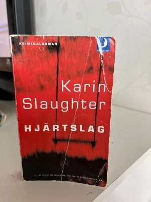 Hjärtslag av Karin Slaughter - Spännande kriminalroman i pocketformat av Karin Slaughter. Omslaget är rött med svart motiv och tydlig vit text. Perfekt för dig som gillar nervkittlande deckare och vill ha något riktigt fängslande att läsa.