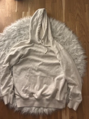 Beige hoodie med magficka och huva - Säljer en enkel och stilren beige hoodie med  magficka och dragsko i huvan. Hoodien har ribbade muddar vid ärmslut och nederkant. Perfekt för en avslappnad och chill look.