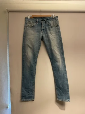 Dondup jeans - Säljer ett par ljusblå jeans med raka ben och klassisk femficksmodell. Jeansen har slitningar och tvättade detaljer framtill och baktill för en avslappnad look. Tillverkade i denim med normal midja och dragkedja.