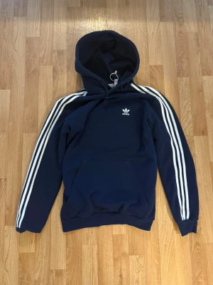 Adidas hoodie mörkblå - Snygg marinblå hoodie från Adidas med en Adidas-logga på bröstet. Hoodien har en magficka framtill. Hoodien är i grymt skick och Perfekt för en sportig och avslappnad stil. Plagget är skickat samma dag det är köpt❤️‍🩹 Pris kan diskuteras vid en snabb affär💨