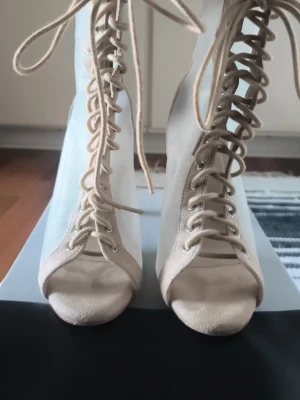 Beige snörade mesh-pumps med öppen tå - Säljer ett par snygga beige pumps med snörning framtill och öppen tå. Skorna har höga klackar och sidor i transparent mesh som ger en modern look. Perfekta för dig som vill sticka ut med ett par unika klackar i garderoben.