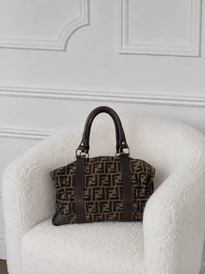 Fendi handväska - Säljer en brun handväska från Fendi med det klassiska FF-monogrammet i canvas och detaljer i mörkbrunt läder. Väskan har två robusta handtag och förstärkta hörn i läder. Perfekt för dig som gillar lyxiga accessoarer med ikonisk design. Varan har tecken på användning men den har blivit väl omhändertagen. Fler bilder kan skickas privat samt äkthetsbevis.