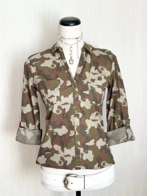 Camouflage skjorta med knappar - Snygg camouflage-mönstrad skjorta med knappar framtill och klassisk krage. Skjortan har långa ärmar som kan vikas upp och fästas med knapp. Perfekt för dig som gillar streetwear eller vill sticka ut lite extra.