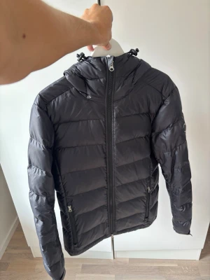 Svart glänsande j.lindeberg dunjacka  - Supersnygg svart dun vinter jacka från J.lindeberg av högsta kvalité och storlek S säljes. Galet snygg och grym passform perfekt nu till vintern. Använt men mycket bra skick och nypris på över 4000 kr. Jackan är i superfint skick inga hål eller fläckar