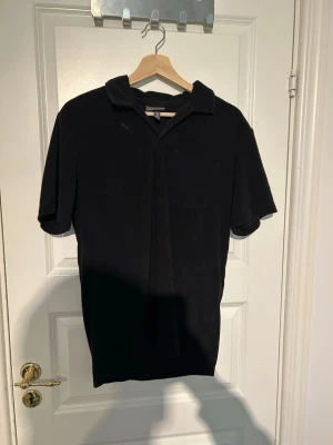 Svart kortärmad henley skjorta M - Säljer en svart henley skjorta i storlek M. Skjortan har korta ärmar, klassisk krage och en enkel bröstficka. Tillverkad i mjukt bomullsmaterial som känns skönt mot huden. Perfekt för en avslappnad och stilren look.