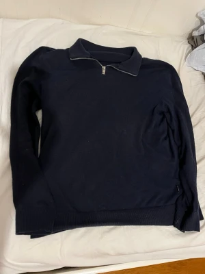 Mörkblå stickad quarterzip-tröja - Snygg mörkblå stickad tröja från Jack & Jones med halvzip och krage. Tröjan har långa ärmar och ribbade muddar vid ärmslut och nederkant. Perfekt för lager på lager och enkel att matcha med jeans eller chinos.