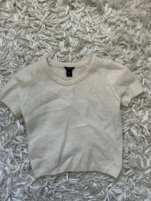 Vit stickad kortärmad tröja Lindex - Säljer en vit stickad tröja från Lindex med korta ärmar och rund halsringning. har en passform som en lös tshirt.