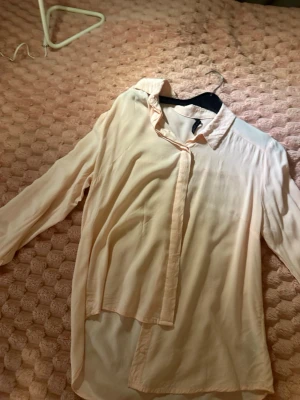 Ljusrosa blus med krage - Säljer en ljusrosa blus med klassisk krage och knäppning framtill. Blusen har långa ärmar och är tillverkad i ett tunt, mjukt tyg som faller snyggt. Perfekt att styla med jeans eller kjol för en trendig look.