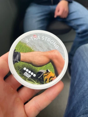 MUF X-TRA STRONG snusdosa - Säljer en vit snusdosa med texten X-TRA STRONG och motiv av ett ben vid en sjö. Dosan har tryck från MUF och politiska budskap på undersidan. Perfekt för dig som gillar unika eller politiska snusdosor.