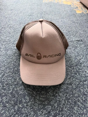 Beige och brun keps från Sail Racing - Grå Sail Racing keps 🩶 Storlek One Size. Snygg och enkel keps som passar till det mesta. Fint skick!