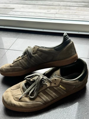 Adidas Samba sneakers beige/grön - Säljer ett par Adidas Samba sneakers i beige mocka med gröna detaljer och gummisula. Klassisk låg modell med snörning och guldfärgad SAMBA-text på sidan. Perfekta för dig som gillar retrostil och streetwear.