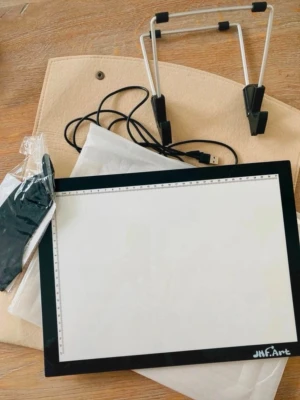JHF.Art LED Light Pad Kit – New - JHF.Art ultra-thin LED Light Pad Kit, perfect for artists, designers, crafters, and hobbyists. The bright backlit surface makes tracing, drawing, diamond painting, quilting, and other creative projects easy and precise.  The kit includes:  * Ultra-thin LED light pad with built-in measuring rulers * Adjustable metal stand for comfortable working * USB power cable * Felt storage sleeve for protection and easy transport * Artist smudge glove  Condition: New Price: For 1 piece Original/new price: Ov