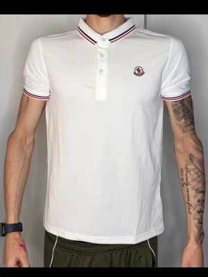Vit Moncler piké med rödblå detaljer - Säljer denna fina Moncler Piké i bra skick.   Storlek: [M men sitter som S] Skick: [mycket bra] Färg: [vit]  Passform: [Slim] Skickas snabbt och välpackat!