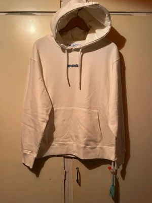 Vit off white hoodie  - Säljer en stilren off white hoodie med huva och dragsnören. Hoodien har en stor magficka och ribbade muddar vid ärmar och nederkant. Perfekt för en avslappnad och trendig look. Den helt ny.