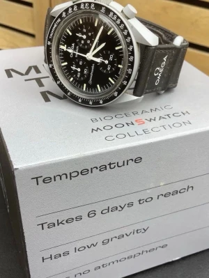 Omega x Swatch MoonSwatch svart klocka - Säljer en Omega x Swatch MoonSwatch med svart urtavla och svart textilband. Klockan har kronograf, tachymeter och tydliga vita visare. Boetten är i ljusgrå biokeramik och bandet har Omega-logga. Perfekt för dig som gillar ikonisk design.