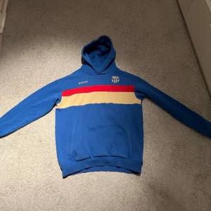 Blå Barça hoodie med röd och beige rand - En Barcelona tröja från 2022 som är väldigt snygg. Använd 2-3 gånger väldigt bra skick. Säljer för 300 kr! Möjligtvis kan godkänna ner till 180 kr!