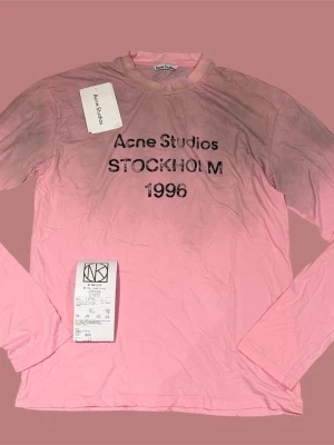 Rosa långärmad topp Acne Studios - Långärmad rosa topp från Acne Studios med tryck 'Acne Studios STOCKHOLM 1996' på bröstet. Tillverkad i mjuk bomull och har en klassisk rund halsringning. Perfekt för dig som gillar stilrena och trendiga plagg. Tillkommer med kvitto 