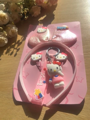 Hello Kitty rosa håraccessoarset - Sött håraccessoarset i rosa med Hello Kitty-tema. Innehåller ett diadem med glitterrosett, två hårspännen med Hello Kitty-huvuden och en nyckelring med Hello Kitty-figur. Perfekt för dig som älskar gulliga detaljer och vill piffa till frisyren med något extra.