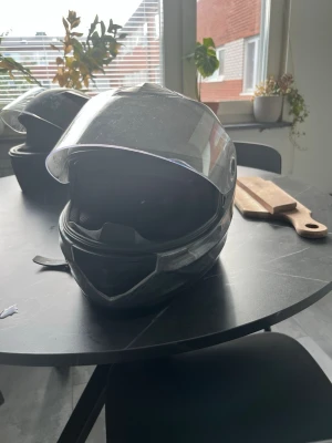 Grå MC hjälm. - Säljer en grå integralhjälm med klart visir och sportig design. Hjälmen har ventilationsöppningar och ett modernt utseende, perfekt för motorcykel eller moped. Tillverkad i hårdplast med mjuk insida för extra komfort. Är dock väldigt användt som man kan se på utsidan. Men fungerar fortfarande utmärkt.