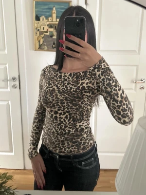 Leopardmönstrad långärmad topp - Snygg långärmad topp med leopardmönster i beige, svart och bruna toner. Figurnära passform och rund halsringning. Perfekt för dig som vill sticka ut med ett djurmönstrat plagg.