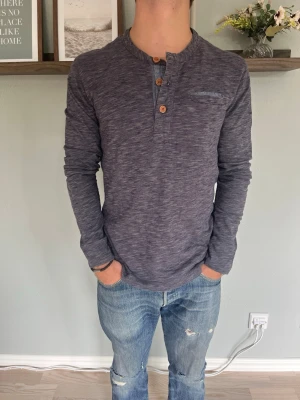 Selected Homme Henley Långärmad Tröja Grå/Marinblå S - Selected Homme henley i melerad grå/marinblå jersey, med knappstängning vid halsen och bröstficka. Avslappnad passform, mjukt material.  Skick: bra skick, inga hål eller fläckar Material: se innertagg för materialmix Storlek: S Modell: 175 cm / 65 kg — sitter true to size på bild