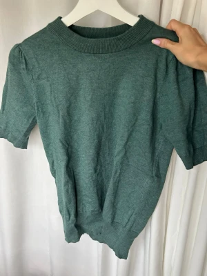 Grön stickad tröja Saint Tropez - Mysig grön stickad tröja från Saint Tropez med korta puffärmar och ribbade muddar vid hals, ärmslut och nederkant. Perfekt till jeans eller kjol för en avslappnad men ändå stilsäker look.