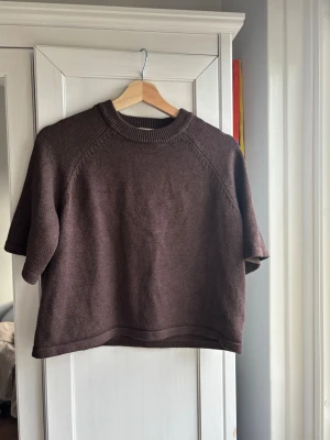 Brun stickad tröja med kort ärm - Skicka gärna bud!                                          Mörkbrun stickad tröja med korta ärmar och rund halsringning. Tröjan har en boxig passform och ribbstickade detaljer vid halsen. Perfekt för lager på lager och enkel att styla till olika outfits.
