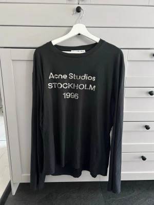 Acne Studios long sleeve  - Svart långärmad t-shirt från Acne Studios med trycket 'Acne Studios STOCKHOLM 1996' på bröstet. Klassisk rund hals och relaxed fit. Perfekt för dig som gillar stilrena och tidlösa plagg med en touch av streetwear.