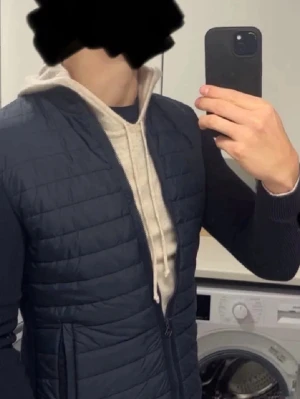 Mörkblå quiltad cardigan med dragkedja - Snygg mörkblå cardiganjacka med quiltat framstycke och stickade ärmar. Jackan har hel dragkedja framtill, ståkrage och två sidofickor med dragkedja. Perfekt för lager-på-lager och ger en sportig look.
