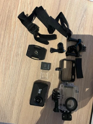 Svart actionkamera 4K GEAR - Actionkamera i svart plast med 4K-upplösning från GEAR. Medföljer vattentätt hus, fästen, remmar och minneskort. Kompakt och rektangulär design, perfekt för äventyr och sport. Linsen sitter framtill och kameran har flera tillbehör för montering.