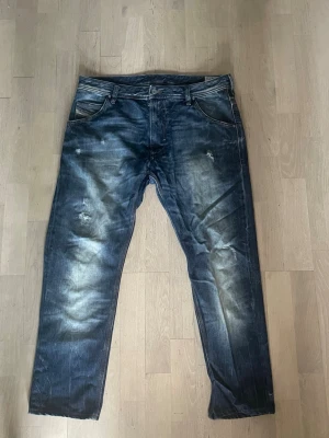 Mörkblå diesel jeans med tvättade detaljer 34/34 - Säljer ett par mörkblå jeans med snygga slitningar och tvättade effekter på benen. Klassisk femficksmodell med raka ben och normal midja. Jeansen har kontrastsömmar och är tillverkade i denim, perfekt för en avslappnad och trendig look.