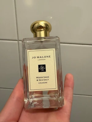 Jo Malone Wood Sage & Sea Salt - Fräsch och elegant parfym från Jo Malone, Wood Sage & Sea Salt. Flaskan är rektangulär i genomskinligt glas med en lyxig guldfärgad rund kork. Doften är inspirerad av hav och skog, perfekt för dig som gillar naturliga och fräscha toner. Säljs för 800