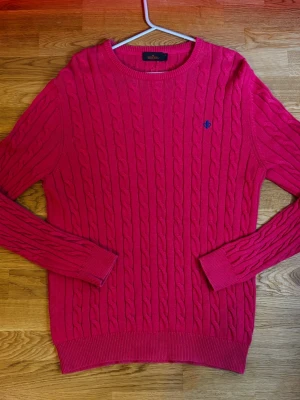 Morris - galet snygg kabalstickad röd/rosa tröja - Riktigt snygg röd/rosa kabelstickad tröja från Morris med rund halsringning och diskret blå logga broderad på bröstet. Tröjan har långa ärmar och ribbade muddar vid ärmslut och nederkant. Perfekt för dig som gillar klassisk och stilren look. Den är XL, men skulle säga att den passar även M-L. Riktigt snygg att bara ha som den är eller med en schysst skjorta under. Färgen är riktigt SNYGG! ✨