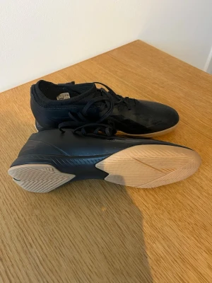 Svarta inomhusskor med gummisula - Säljer ett par svarta inomhusskor från Adidas  med låg profil och snörning. Skorna har en ljus gummisula som ger bra grepp på inomhusgolv. Använda ett fåtal gånger för att spela fotboll inomhus. Kostade över 1000kr vid inköp. 