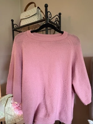 Rosa stickad tröja från 157 - Mysig rosa stickad tröja från 157 med rund halsringning och avslappnad passform. Tröjan har ribbstickade muddar vid halsen och ärmarna, perfekt för lager-på-lager och chill dagar.