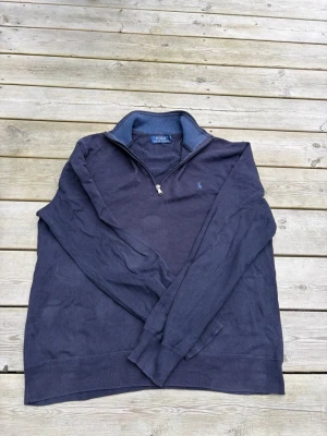 Mörkblå halvzip tröja Polo Ralph Lauren - Mörkblå långärmad tröja från Polo Ralph Lauren med halvzip och liten broderad logga på bröstet. Tröjan har ribbade muddar vid ärmslut och nederkant samt en mjuk insida vid kragen. Perfekt för en avslappnad men stilren look. 