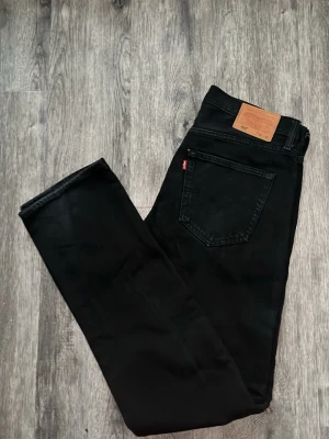 501 - Säljer ett par svarta jeans från Levi's med klassisk rak passform och femficksmodell. Jeansen har en läderpatch bak i midjan och den ikoniska röda Levi's-taggen på bakfickan. Perfekta till en avslappnad streetstyle-look.