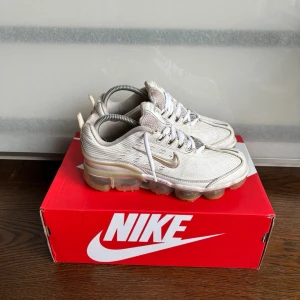 Nike Vapor Max 360 vita sneakers - Nike Air Max 360 sneakers i vitt med silvriga och beige detaljer. Skorna har en futuristisk design med synlig Air-sula runt hela foten, mesh och syntetmaterial i ovandelen samt klassisk Nike Swoosh på sidan. Perfekta för dig som gillar streetwear och sportig stil.
