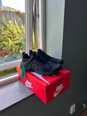 Nike helsvarta sneakers - Snygga helsvarta Nike sneakers med låg profil och sportig design. Skorna har en ovandel i mesh och syntet, med matchande svarta snören och sula. Perfekta för dig som gillar en clean och stilren look till vardagsoutfiten.