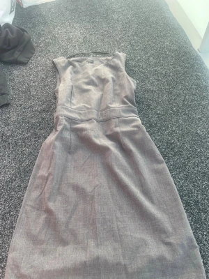 Brun rutig klänning från Lindex - Snygg grå klänning från Lindex med diskret rutigt mönster. Klänningen har en klassisk, figurnära passform och är ärmlös med rund halsringning. Perfekt till många olika tillfällen och enkel att styla med accessoarer.