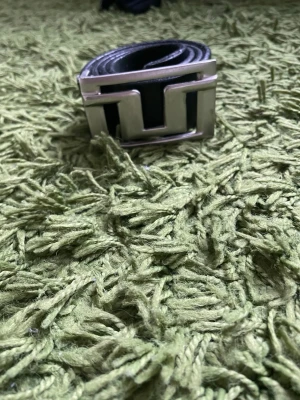 Svart bälte med stor silverspänne - Snyggt svart bälte med ett brett, geometriskt silverspänne som verkligen sticker ut. Perfekt accessoar för att lyfta vilken outfit som helst och ger en cool touch till din stil. Bältet är i skinn och har en modern design.