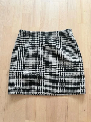 Rutig ull kortkjol från H&M - Snygg svartvit rutig kortkjol från H&M i klassiskt mönster. Kjolen har en rak passform och är fodrad för extra komfort. Perfekt att matcha med en enkel topp eller stickad tröja.