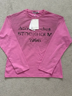 Rosa Acne Studios longsleeve - Säljer en rosa långärmad topp från Acne Studios med tryck i svart text på bröstet där det står 'STOCKHOLM 1996'. Passar dig som är 160-175 cm. Priset går självklart att förhandla 🤗
