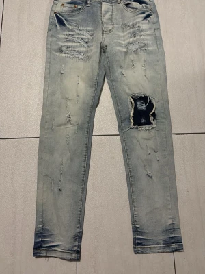 Purple jeans - Säljer ett par ljusblå jeans från Purple Brand med slitningar och stora hål på ena benet. Jeansen har skinny fit och klassisk femficksmodell. Materialet är denim i bomull med snygg tvätt och slitna detaljer för en trendig look. Jag har tappat bort purple taggen också