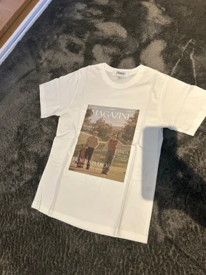 Vit t-shirt med magazine-tryck - Säljer en stilren och snygg T-shirt med tryck från Fiore Studios   T-shirten är vit med ett snyggt vintageinspirerat magasintryck framtill. Enkel att matcha och passar perfekt till både jeans och shorts.  Bilderna / trycket är gjort med presstekniken sublimering. Vilket betyder att trycket färgas i själva fibrerna / trådarna på tyget och INTE som ett plastigt lager ovanpå tyget.   Storlek: XS - Aldrig använd