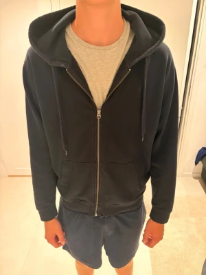 Replay  - En enkel och stilren mörkblå hoodie med dragkedja framtill och två fickor. Tröjan är från Replay och har justerbara snören i huvan och ribbade muddar vid ärmar och nederkant. Perfekt för hösten då den är lite varmare och lite mörkare i färgen. 