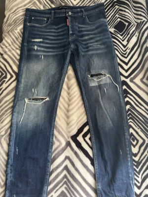 Blå slitna jeans - Säljer ett par blå Jeansen har en tvättad look med ljusare partier och klassisk femficksmodell. Perfekta för dig som gillar en avslappnad och trendig stil.