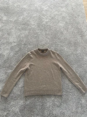 Beige stickad tröja med rund hals - Mysig beige stickad tröja med rund halsringning och långa ärmar. Tröjan har ribbade muddar vid ärmslut och nederkant, vilket ger en klassisk och stilren look. Perfekt för lager på lager under kyliga dagar. Tveka inte på att höra av dig vid frågor!